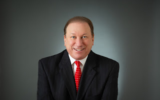 Rick D. Smith, Founder of NewsUSA Inc., professional headshot in navy suit and red tie